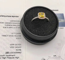 Load image into Gallery viewer, A cushion-cut yellow diamond ring with a halo setting in a black circular display box, placed on top of a gemstone certification report.