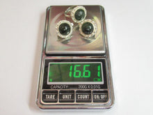 Load image into Gallery viewer, A pair of silver-toned rings with oval dark green stones and textured halo settings, displayed on a digital pocket scale showing 16.61 grams.