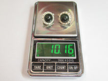 Load image into Gallery viewer, A pair of silver-toned stud earrings with oval black stones and textured silver settings, displayed on a digital pocket scale showing a weight of 10.16 grams.
