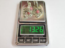 Load image into Gallery viewer, A pair of silver-toned earrings with pink stone accents displayed on a digital scale showing a weight of 13.26 grams.

